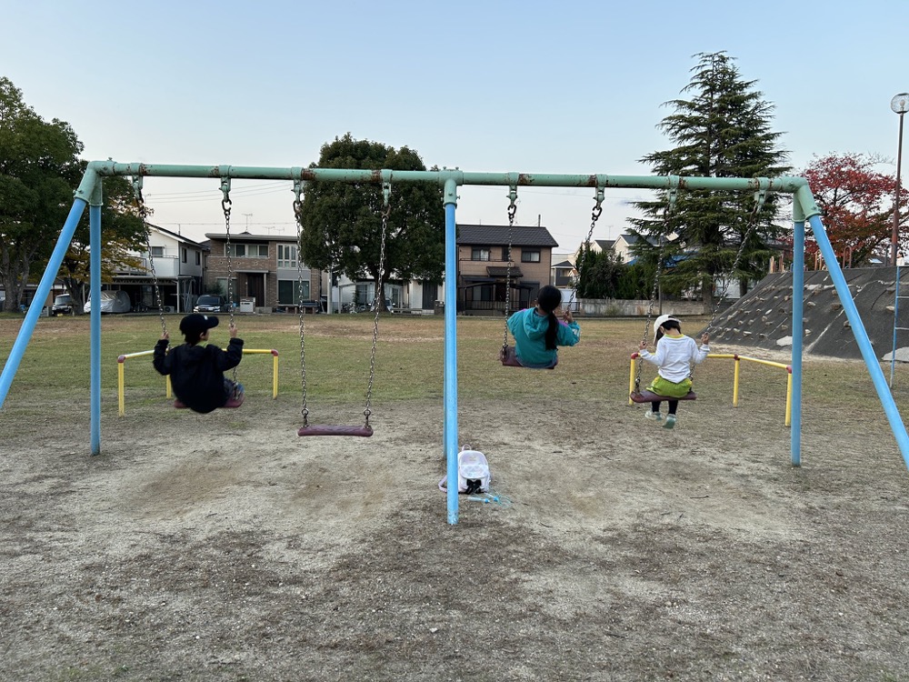 夕方の公園でブランコに乗る3人の子ども